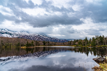 Beautiful lake reflecting blue sky like a mirror, rolling mountain range and woodland in the background on springtime sunny day. High latitude country natural beauty scenery