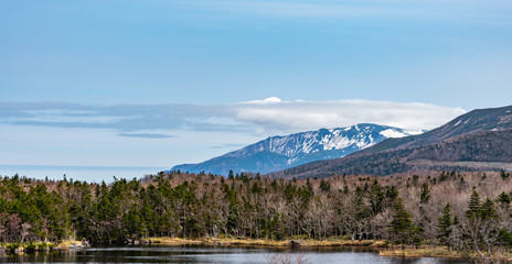 Beautiful lake reflecting blue sky like a mirror, rolling mountain range and woodland in the background on springtime sunny day. High latitude country natural beauty scenery