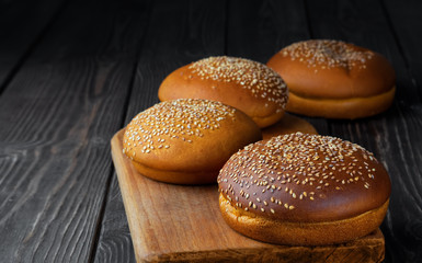 Freshly baked hamburger buns with sesame on dark wooden background. Round bun with sesame or bread rolls. Closeup