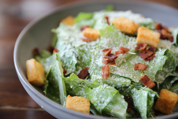 Caesar salad with crispy bread and bacon close up on wood background