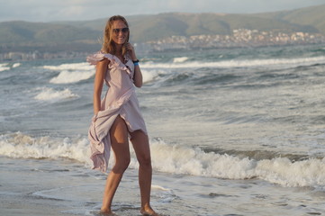 Young girl on the sea beach in a dress, evening wave and wind light, joyful mood.
