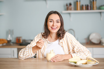 Young woman eating tasty yogurt at home