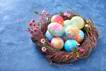 Nest with beautiful Easter eggs on color background