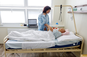 Woman without hair after chemotherapy patient lying at hospital bed feeling sad and depressed worried. A friend came to please her. Health care and clinical attention concept.