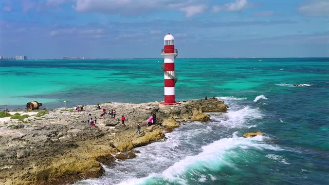 A bride and groom being photographed before their wedding next to a red and white lighthouse. Captured by the Carribean Sea and the Hyatt Ziva in Cancun, Mexico