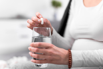 Pregnant woman taking vitamin tablet in a glass of water.