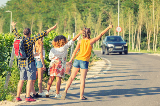 Mixed race group of best friends hitchhiking on the side of countryside road during great summer adventure