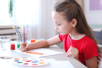 Cute little girl draws paints at home.