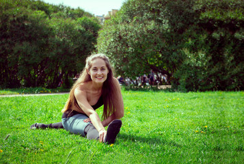 Naklejka na ściany i meble white young woman in sportswear with long hair doing a stretch on the grass in the Park