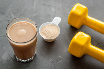 Protein shake in glass near dumbbells on grey background