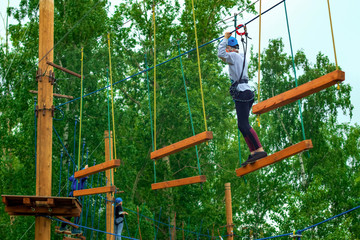 Children in the park in the attraction on the ropes with a safety rope, outdoor activities