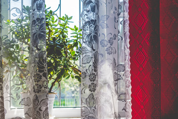 Home large and cozy window from which bright light passes into the room. Apartment fabric interior. Colored and transparent curtains with openwork pattern.