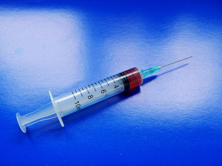 Syringe with medicine and needle, on a blue background close-up.