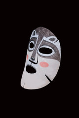 Tissue mask sheet for the face with a raccoon pattern. On a black background. Moisturizing face is nice and fun.