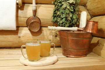 Two glass mugs of light beer in the interior of sauna among copper accessories. 