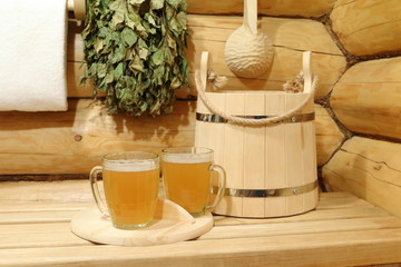 Two glass mugs of light beer among wooden accessories in the interior of sauna.