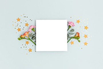 Blank paper card mockup with flowers, eucalyptus and stars confetti. Festive concept with place for text on a blue pastel background.