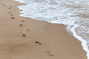 Lonely footprints in beach sand and foam waves
