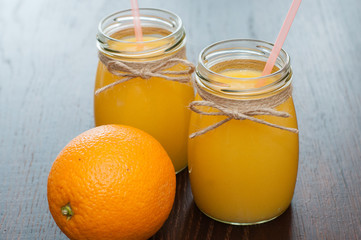 Orange juice and whole orange in two jars rustic style side view, copy space