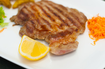 Juicy and delicious grilled meat steak with lemon, carrots, lettuce and potatoes.