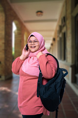 Smiling modern woman in glasses with phone, girl with backpack on outside classroom.