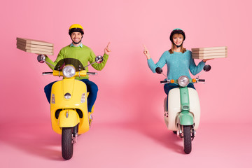 Full body photo of funny lady guy drive two vintage moped carry paper pizza boxes direct finger empty space courier wear casual jumper headgear isolated pink color background
