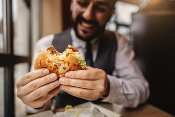 Closeup of hungry man in suit sitting in fast food restaurant and eating cheese burger.