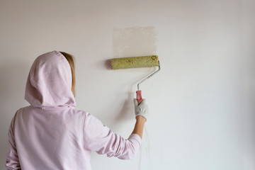 The girl in the hood stands with her back and paints a white wall. Place for text