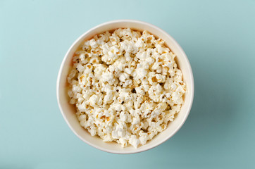 Top view of big bowl of popcorn in the center on the bright blue background