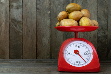 Potatoes on red scales on old wooden background.