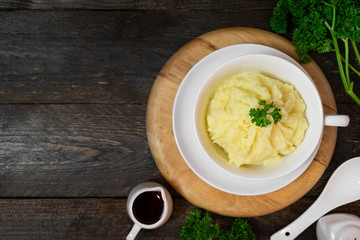 Mashed potatoes in white bowl or glass with parsley on wooden table.