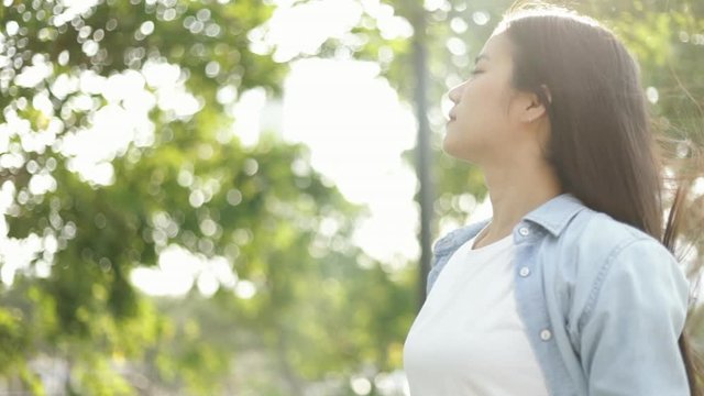 Smile of young asian female relaxed enjoying peaceful sunset and looking up exhaling fresh air relaxing at a public park on the beautiful summer sunset.
