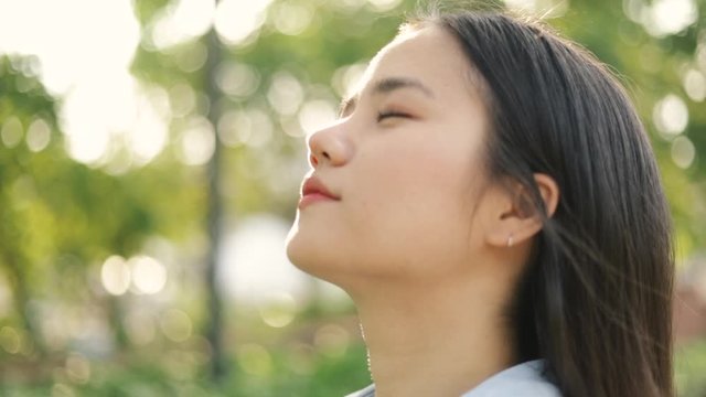 Close up portrait of young asian female relaxed enjoying peaceful sunset and looking up exhaling fresh air relaxing at a public park on the beautiful summer sunset.