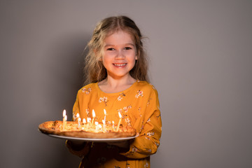 little girl holding pizza with candles is smiling