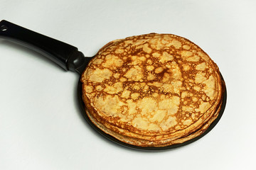 Stack of homemade yeast pancakes on frying pan over white background. Traditional Russian pancake week. Soft focus.