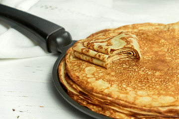 Stack of homemade thin pancakes on a frying pan on white wooden table. Russian pancake week concept. Selective soft focus.