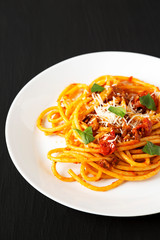 Homemade Bucatini all Amatriciana Pasta in a white plate on a black surface, low angle view. Close-up.