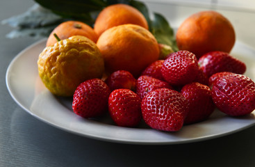 Fresh delicious strawberries and oranges served on white plate and isolated in bright background