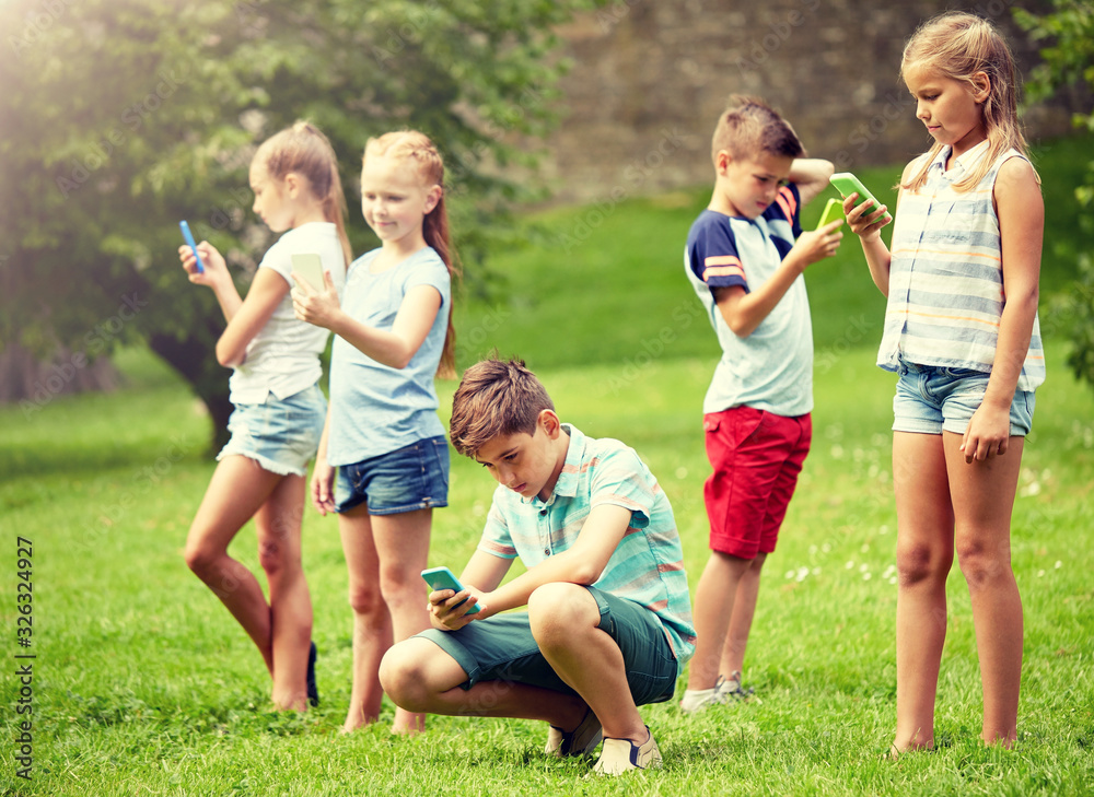 Wall mural childhood, augmented reality, internet addiction, technology and people concept - group of kids or friends with smartphones playing game in summer park