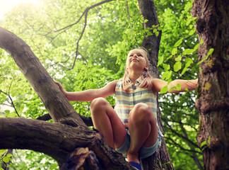 friendship, childhood, leisure and people concept - happy girl climbing up tree and having fun in...