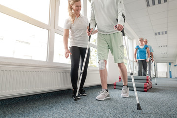 People in rehabilitation learning how to walk with crutches - obrazy, fototapety, plakaty