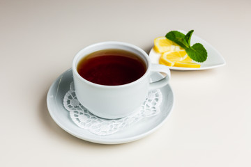 A white cup of black tea on a saucer and paper napkin, a small saucer with sliced lemon and mint