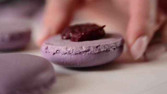 Cooking blueberry macaroons. Woman add filling from the cooking bag. Cooked halves of macaroons lie on a baking sheet. Steps cooking baking macaroon and confectionery.