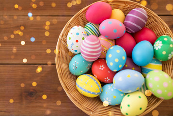 easter, holidays and tradition concept - close up of colored eggs in basket on wooden table
