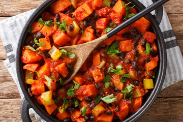 Tasty spicy sweet potatoes and black beans with tomatoes close-up in a pan. Horizontal top view