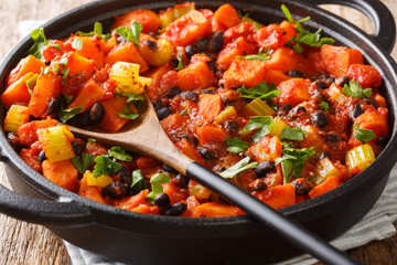 Tasty spicy sweet potatoes and black beans with tomatoes close-up in a pan. horizontal