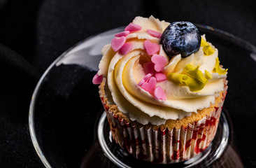 Close-up of gourmet cupcake with buttercream frosting, heart-shaped sprinkles, chips, and blueberry