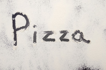 words Pizza written on a black background with flour. Inscription.