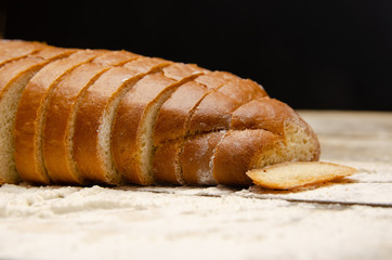Sliced loaf close up on a wooden table with flour on a black background with copy space