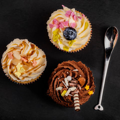 Top view of three different cupcakes close to bizarre teaspoon on dark background
